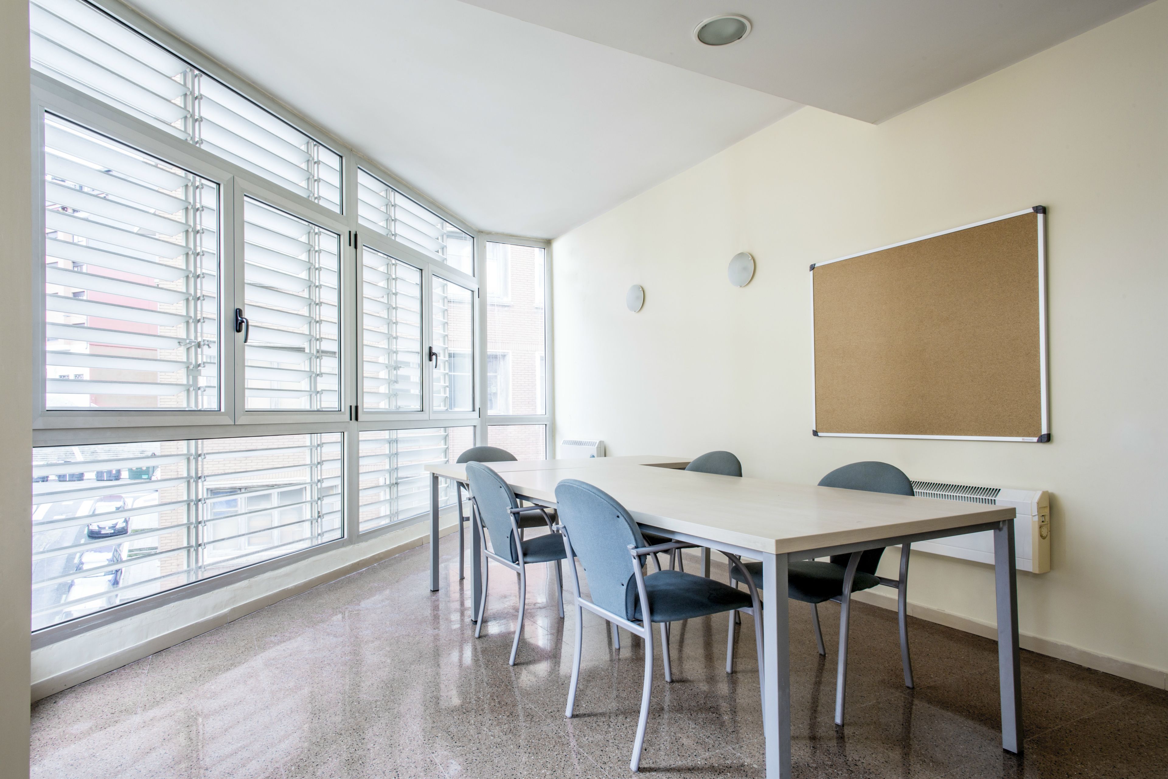 Un salón de conferencias con una gran mesa, cuatro sillas, una pizarra y una ventana con persianas.