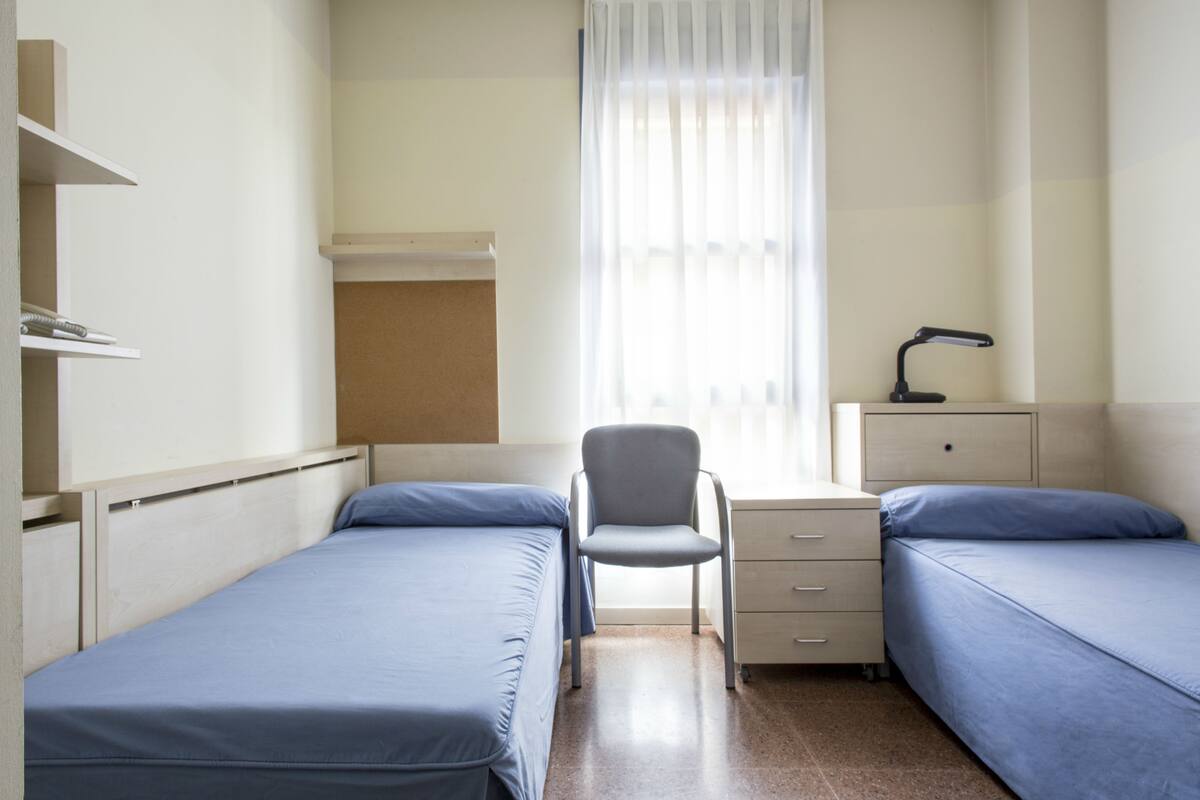 Een slaapkamer met twee eenpersoonsbedden, een stoel, een bureau en een nachtkastje.