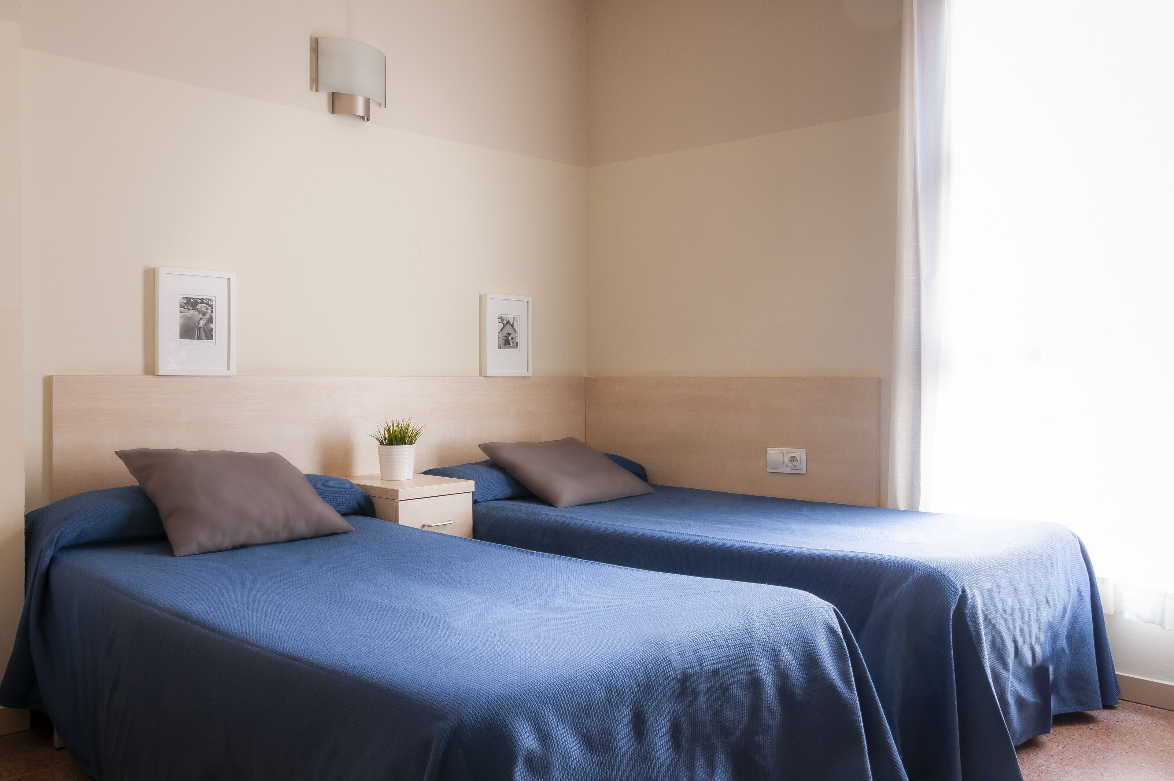 Habitación de hotel con dos camas, una mesita de noche con lámpara y dos cuadros en la pared.