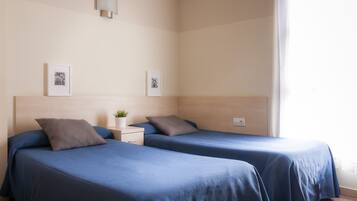 Habitación de hotel con dos camas, una mesita de noche con lámpara y dos cuadros en la pared.