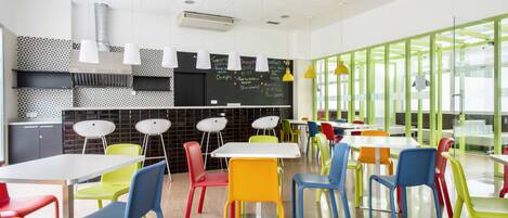 A modern cafeteria with colorful chairs and tables, a chalkboard menu, and a green partitioned area.