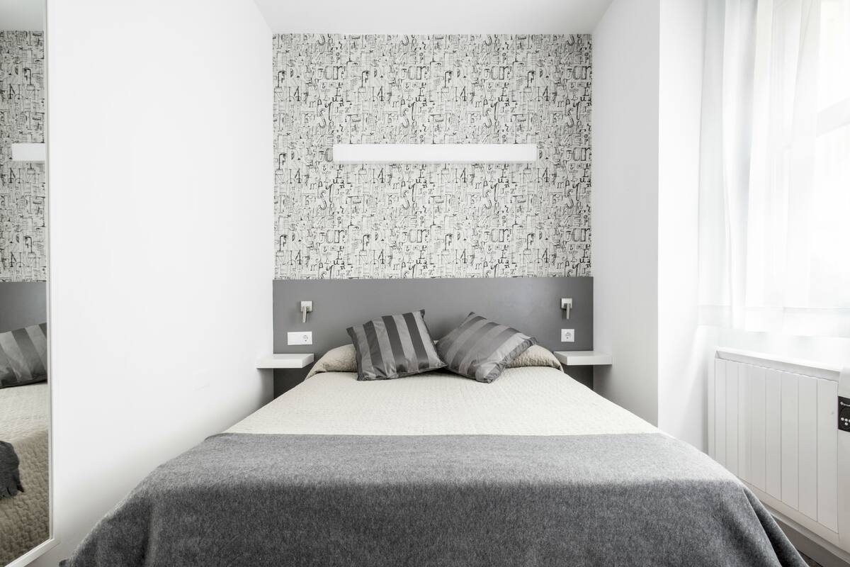 Een moderne slaapkamer met een groot bed, grijze beddengoed en behang met een patroon.