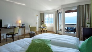 Habitación de hotel con una cama grande, un escritorio, una silla, una mesita con un jarrón y vistas al mar.