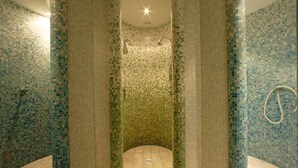Un baño con paredes y suelo de mosaico, una ducha con cabezal de ducha manual y un perchero para toallas.