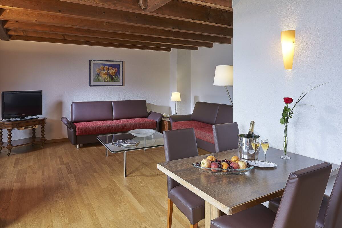 Una sala de estar moderna con techo de madera, un sofá, una mesa de comedor con frutas y bebidas, y un televisor sobre un mueble de madera.