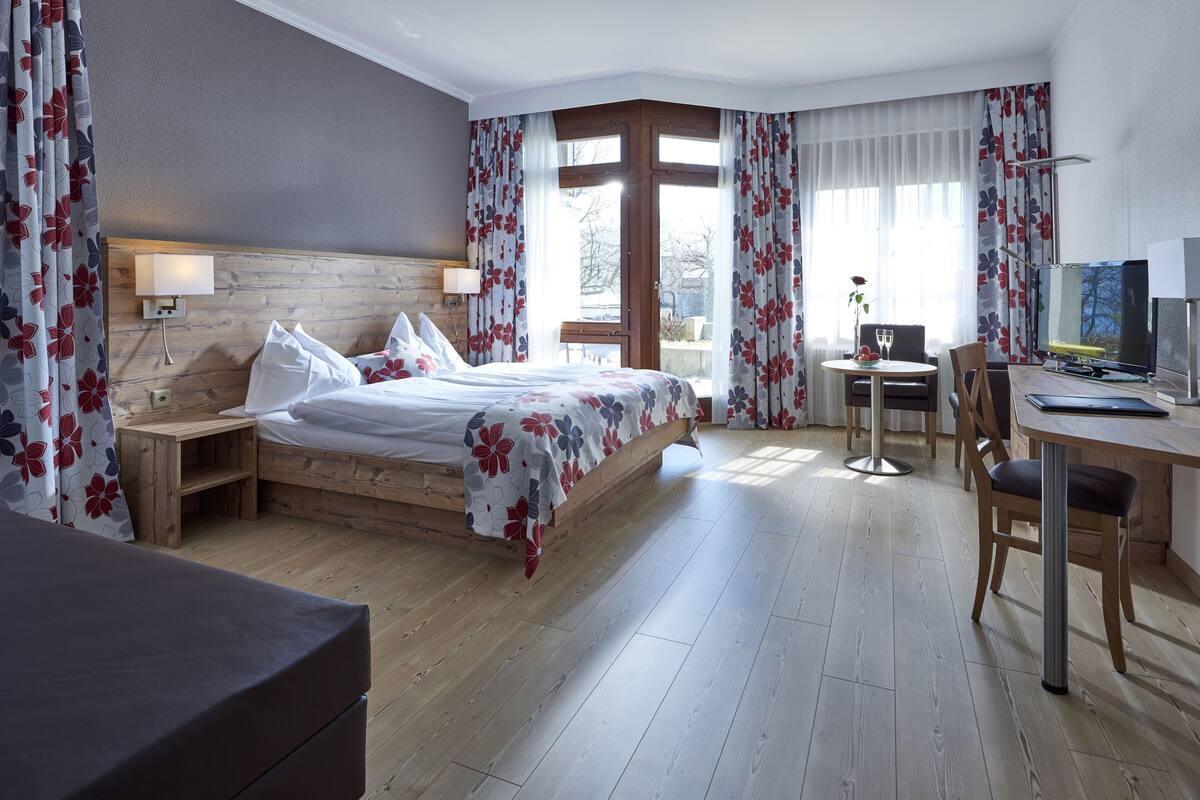 Habitación de hotel con cama, escritorio, silla, televisión y ventana con cortinas.
