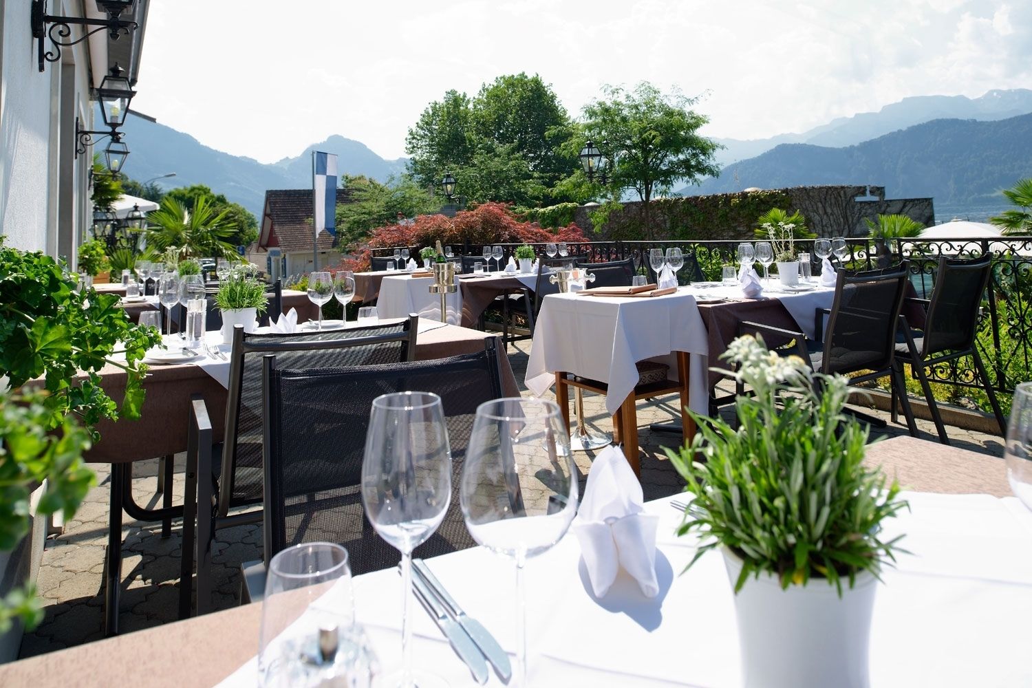 An outdoor dining area with tables set for a meal, surrounded by greenery and overlooking a mountainous landscape.