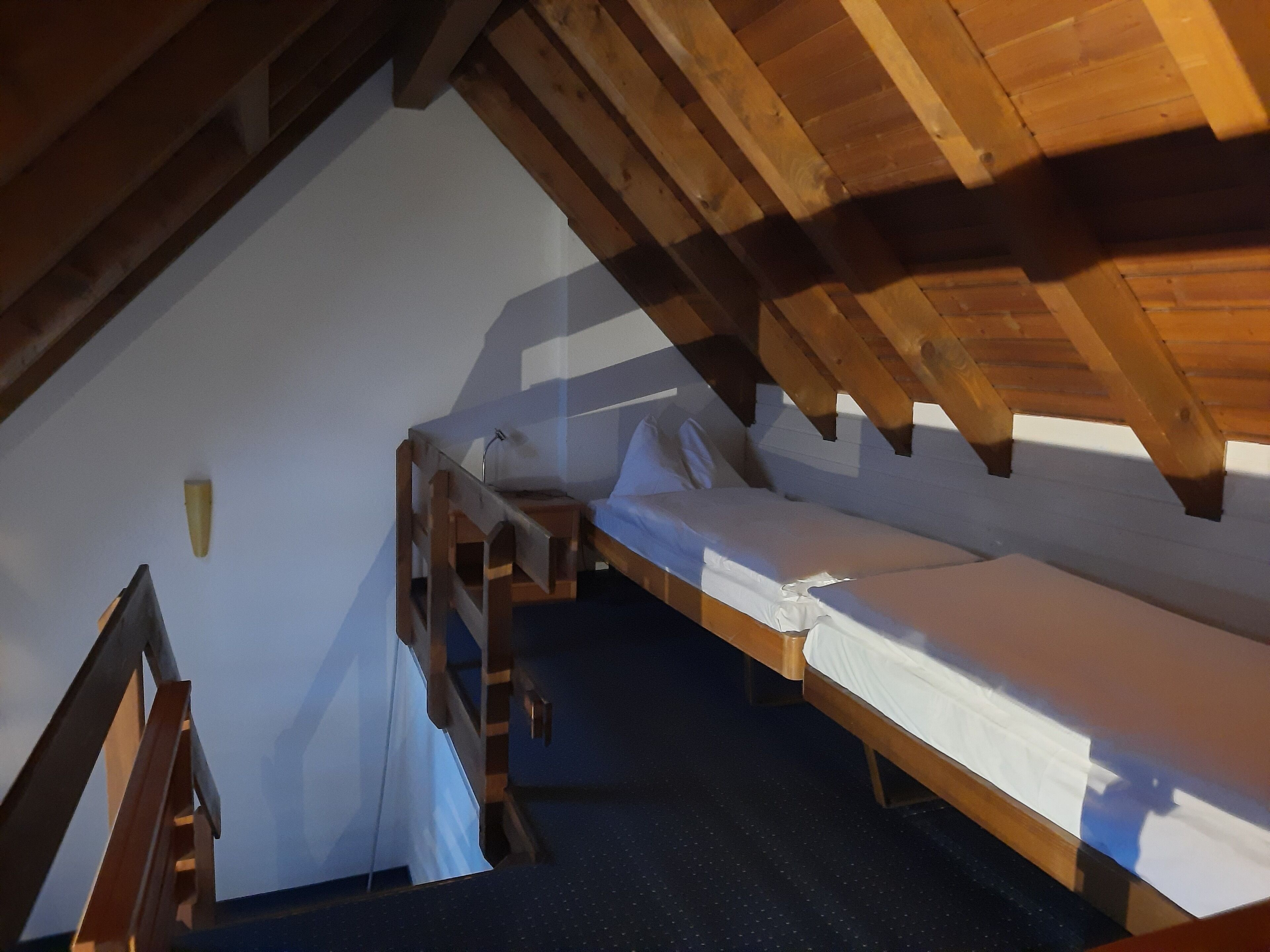 A small, compact room with a sloped ceiling, wooden beams, and a single bed.