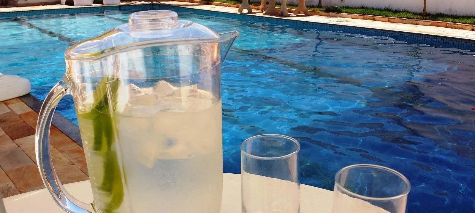 A clear glass pitcher filled with a beverage, placed on a poolside table next to a swimming pool.
