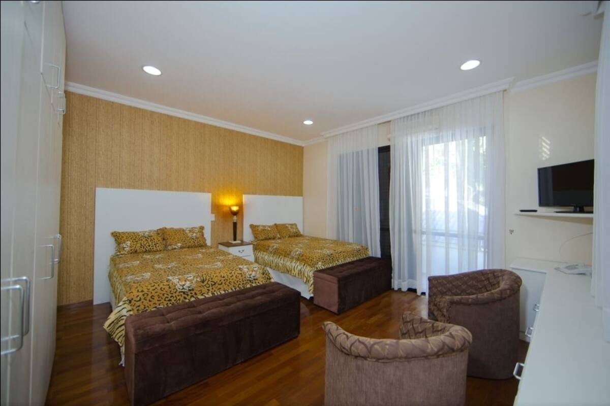 A hotel room with two beds, a sofa, a TV, and a window with curtains.
