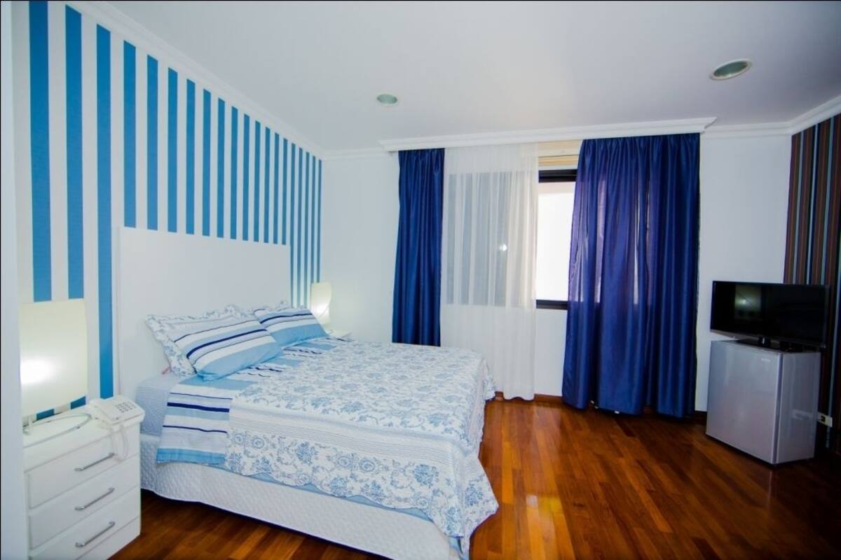 A bedroom with a bed, a TV, a dresser, and a window with curtains.