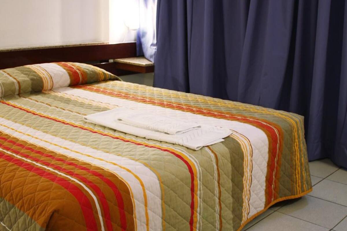 Una cama con colcha acolchada en varios colores, cabecero de madera y una ventana con cortinas.