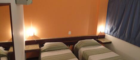 A room with two single beds, a nightstand, a lamp, and a window with a curtain.