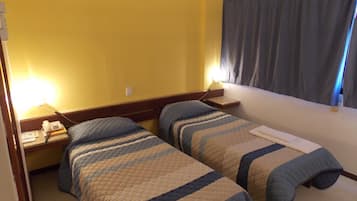 A hotel room with two beds, a bedside table with a phone, and a window with curtains.