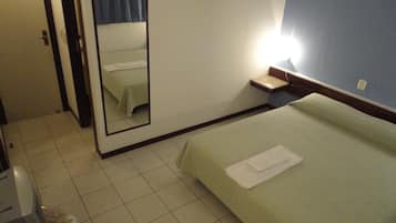 Quarto de hotel com cama, espelho, mesa de cabeceira e uma pequena janela.