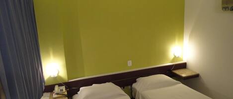 Una habitación de hotel con dos camas individuales, una mesita de noche con lámpara y un espejo grande en la pared.