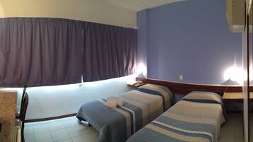 Quarto de hotel com cama, escrivaninha, cadeira, banheiro com pia e vaso sanitário, e cortina.