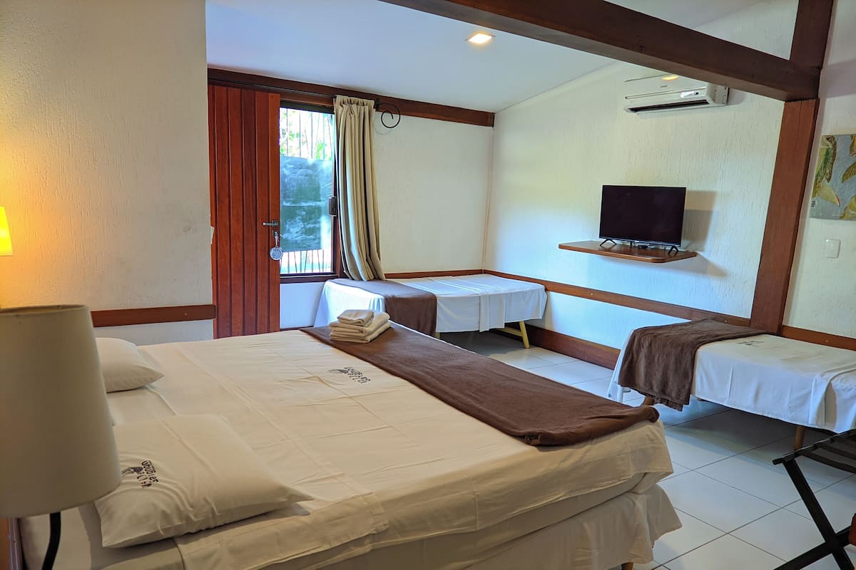 Ein Hotelzimmer mit einem großen Bett, einem Einzelbett, einem Schreibtisch, einem Fernseher und einem Fenster mit Vorhängen.