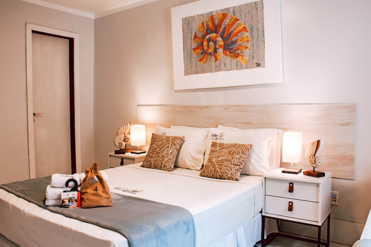 Ein Hotelzimmer mit Bett, Nachttischen, einem Wandbild und einer Tür.
