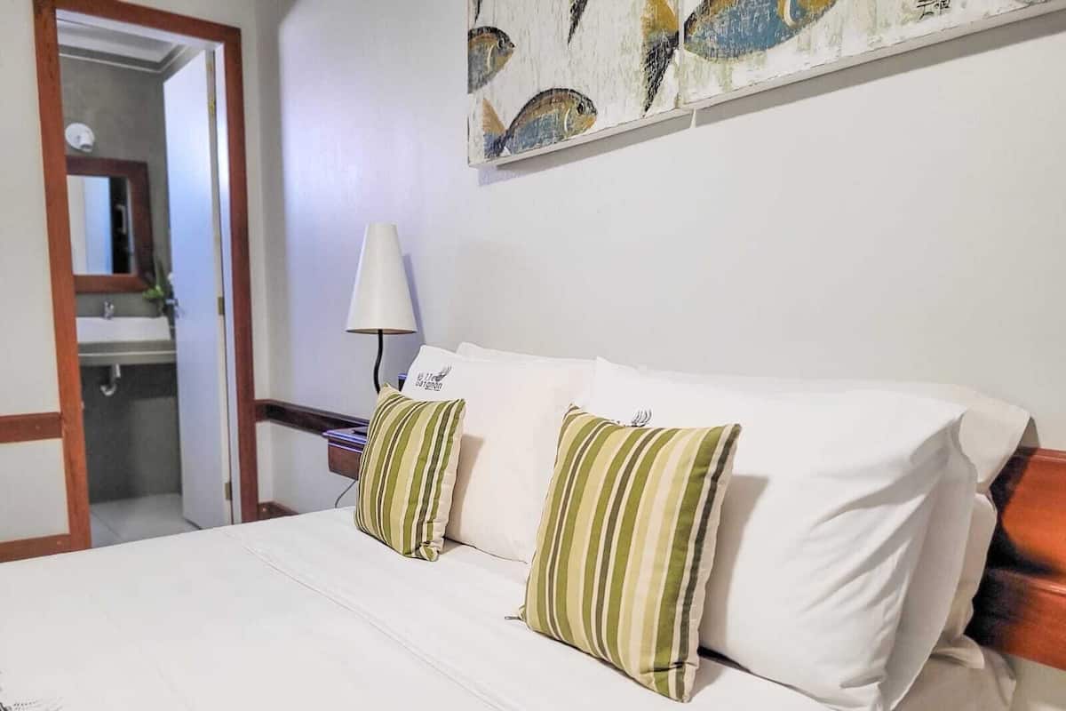 Ein Hotelzimmer mit einem Bett, zwei Kissen, einem Nachttisch mit Lampe und einem Bild an der Wand.