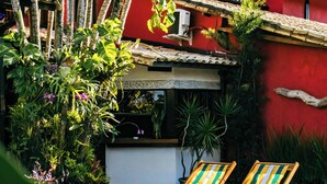 Zona de piscina con dos sillones de descanso, rodeada de exuberante vegetación y un edificio rojo con tejado de tejas.