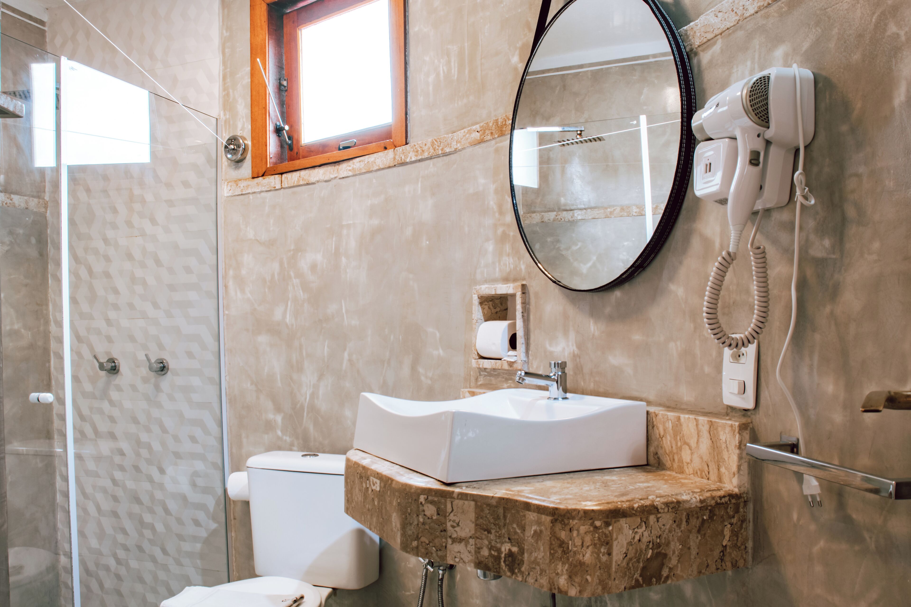 Een badkamer met een glazen douchecabine, een wastafel met een marmeren aanrechtblad, een toilet, een haardroger en een spiegel.