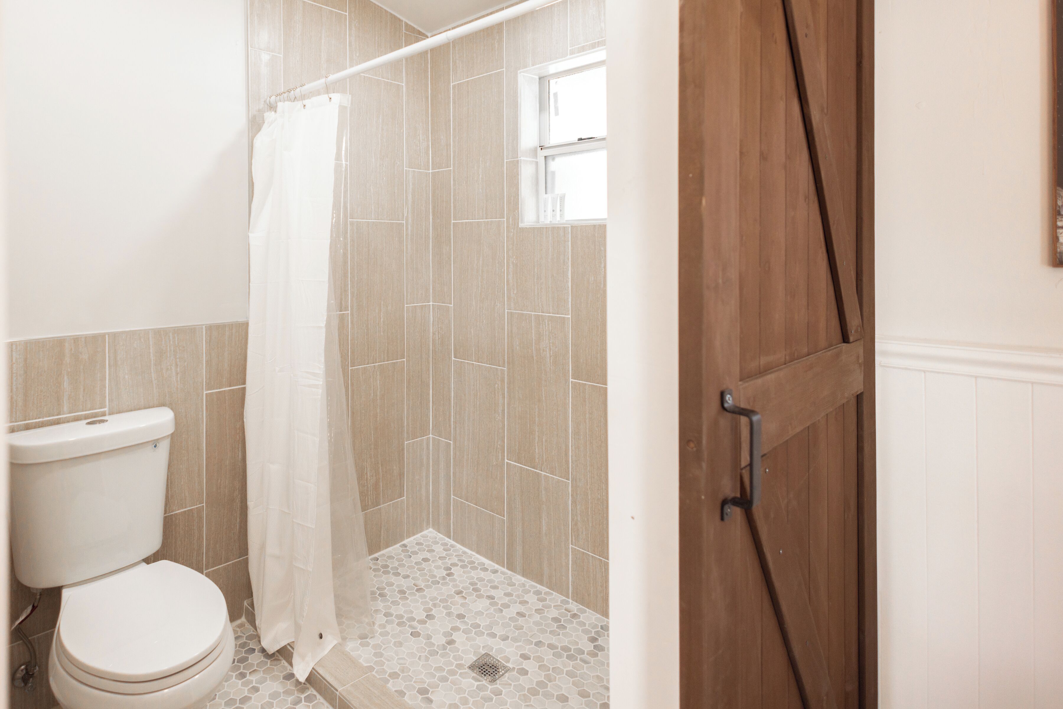 A bathroom with a toilet, shower, and a wooden door.