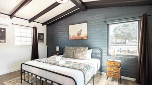 A bedroom with a bed, bedside tables, a window with curtains, and a wall-mounted picture.