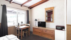 A hotel room with a wooden desk, a television, a microwave, and a dresser.