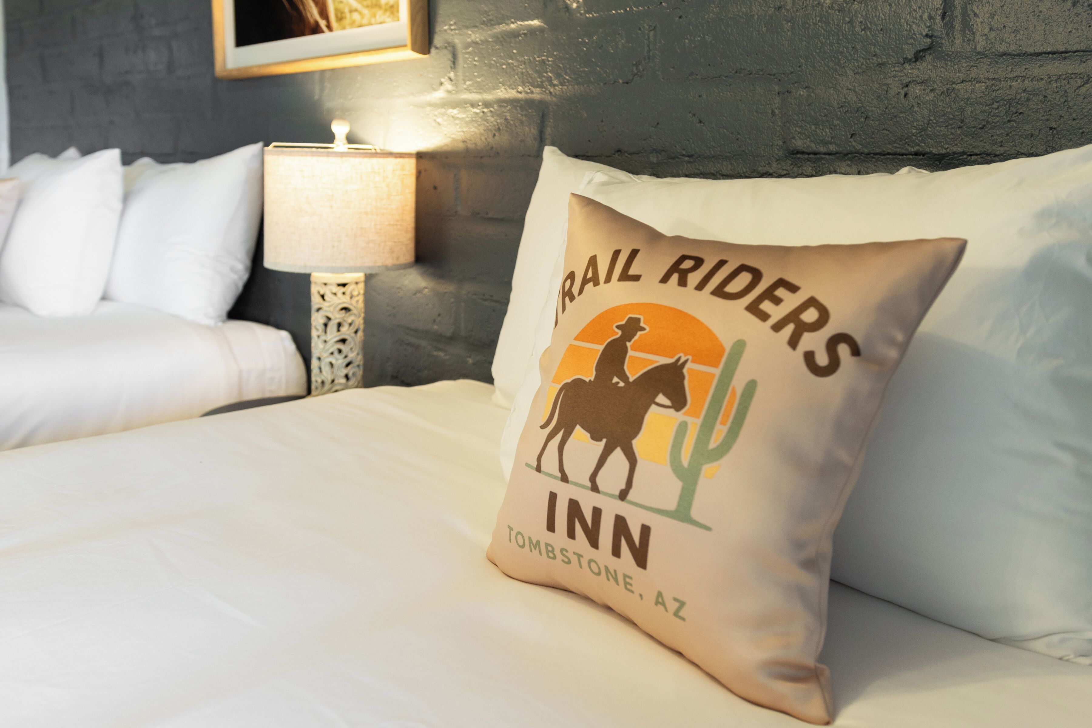 Una cama con un almohadón que muestra el logotipo y el texto de 'Trail Riders Inn' en Tombstone, AZ.