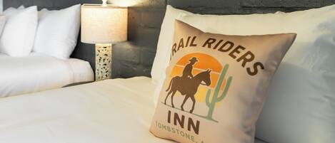 Una cama con un almohadón que muestra el logotipo y el texto de 'Trail Riders Inn' en Tombstone, AZ.