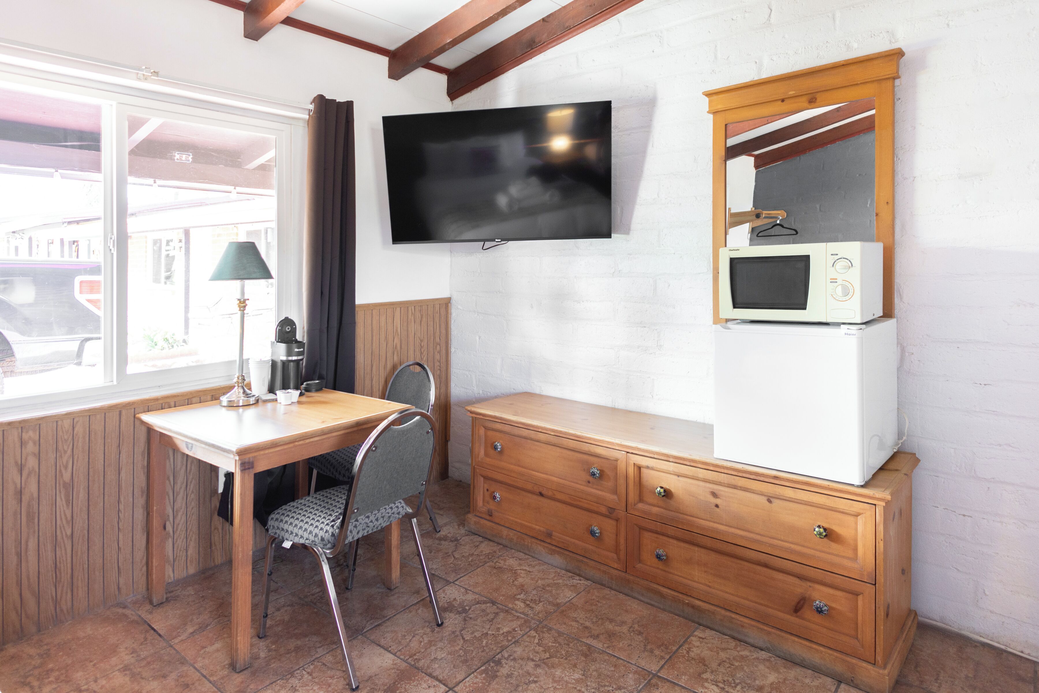 Ein Zimmer mit Schreibtisch aus Holz, einem Stuhl, einem an der Wand montierten Fernseher, einer Mikrowelle und einer Holzkommode.