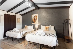 Habitación de hotel con dos camas, un ventanal grande, una pared de ladrillo y una lámpara colgante.