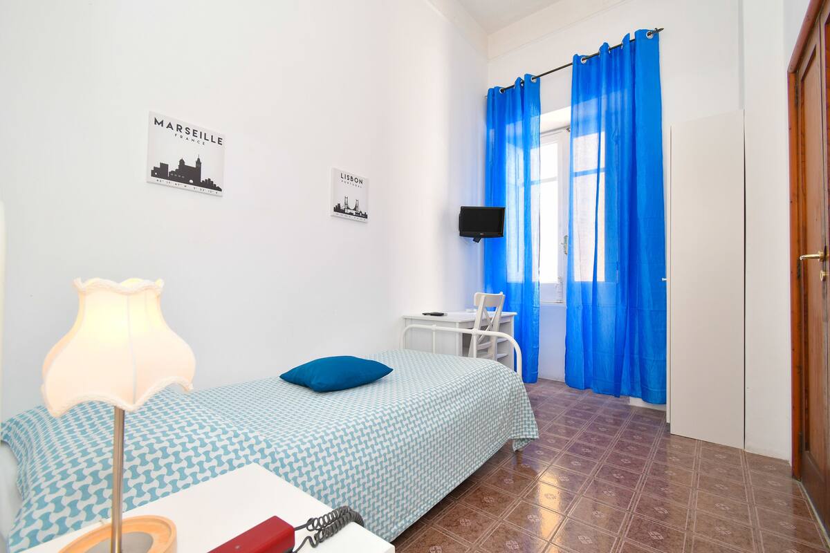 Ein Schlafzimmer mit einem Bett, einem Schreibtisch, einem Sessel, einer Lampe und einem Fernseher.
