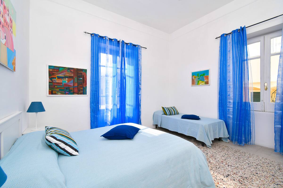 Ein Schlafzimmer mit zwei Betten, blauen Vorhängen und Bildern an den Wänden.
