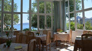 A dining area with large windows, wicker chairs, and tables set for a meal. - Villa Panoramica (Ischia)