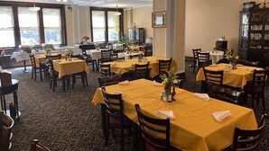A dining area with multiple tables covered with yellow tablecloths, wooden chairs, and a patterned carpet. - The Leo House (New York)