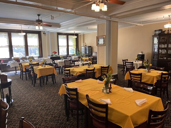 A dining area with multiple tables covered with yellow tablecloths, wooden chairs, and a patterned carpet. - The Leo House (New York)