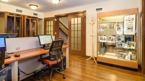 A modern office space with a wooden desk, two computer monitors, a black office chair, and a glass display case with framed photos. - The Leo House (New York)
