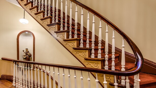A grand staircase with ornate balusters and a polished wooden finish. - The Leo House (New York)