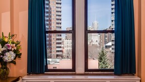 A window with blue curtains, a radiator below, and a vase of flowers on a table to the left. - The Leo House (New York)