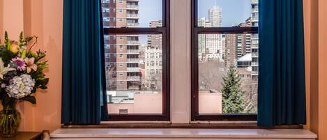 A window with blue curtains, a radiator below, and a vase of flowers on a table to the left.