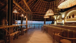 A bar area with wooden furniture, hanging lights, and a view of the ocean. - Hotel Casa Colibri (Playa del Carmen)