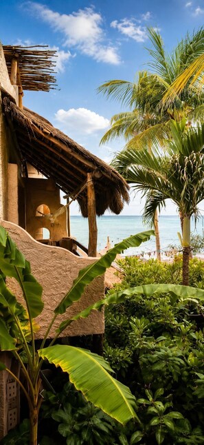 Una casa de playa con techo de paja, vista al océano y vegetación tropical.