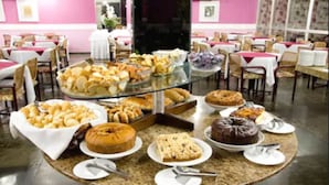 A buffet setup with various baked goods and desserts on display tables in a dining area with pink walls and white tablecloths. - Lanville Athenee (Foz do Iguacu)