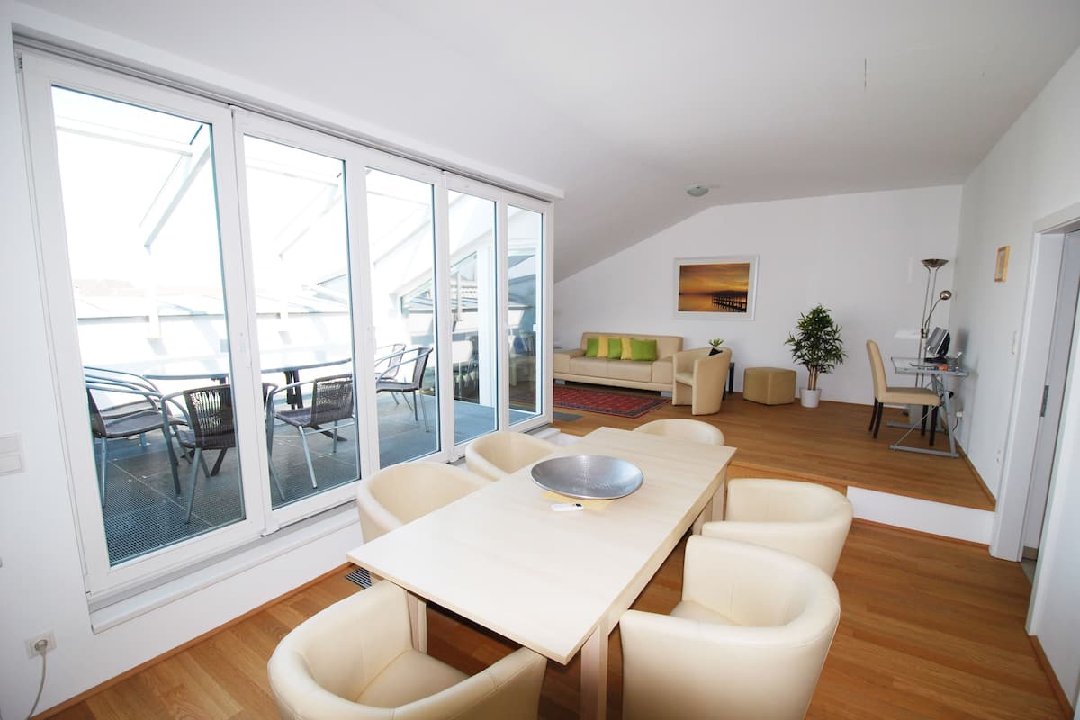 A spacious dining area with a long table and six chairs, large sliding glass doors leading to an outdoor patio, and a cozy living area in the background.