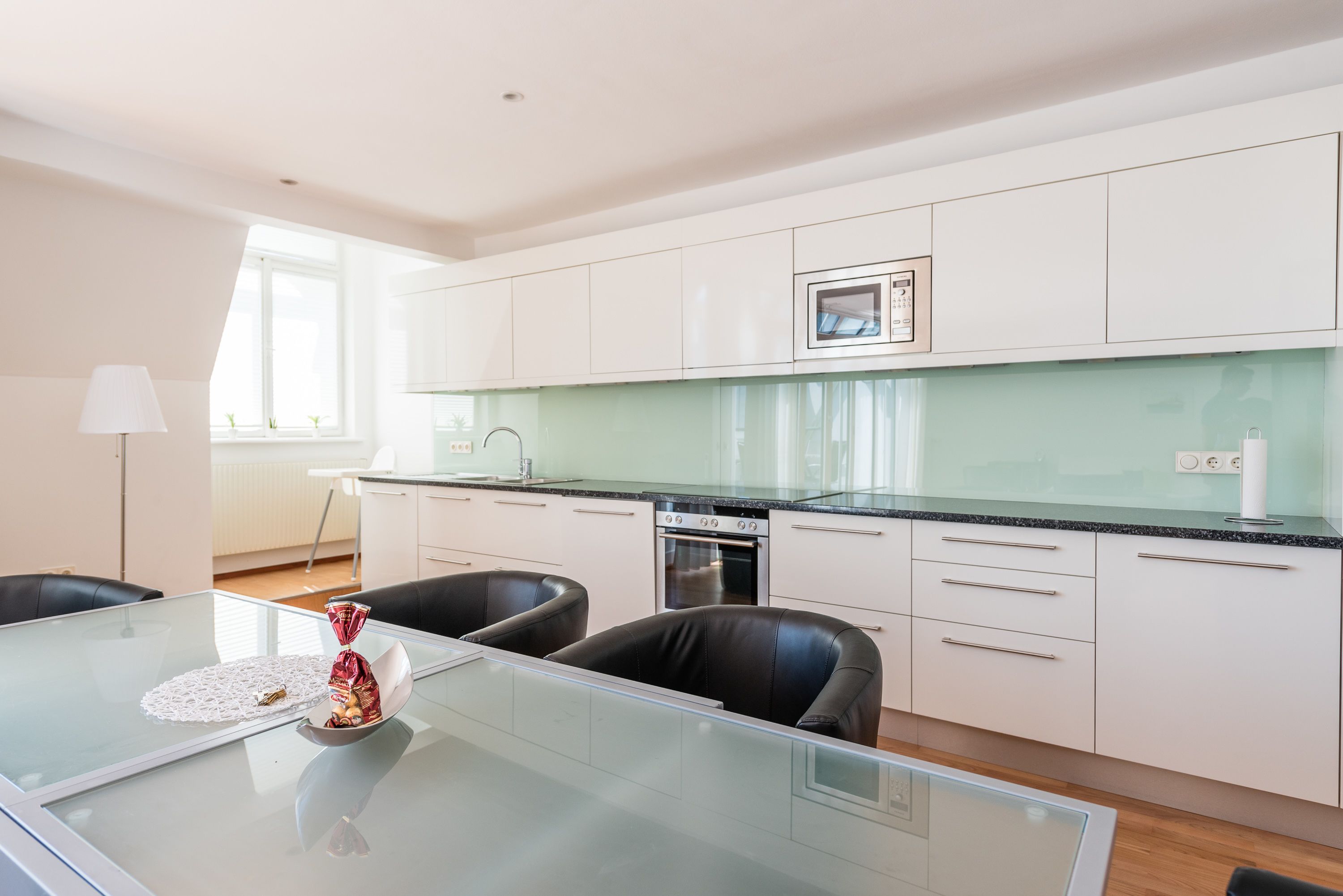 A modern kitchen with white cabinets, a glass-top table, and a built-in oven.