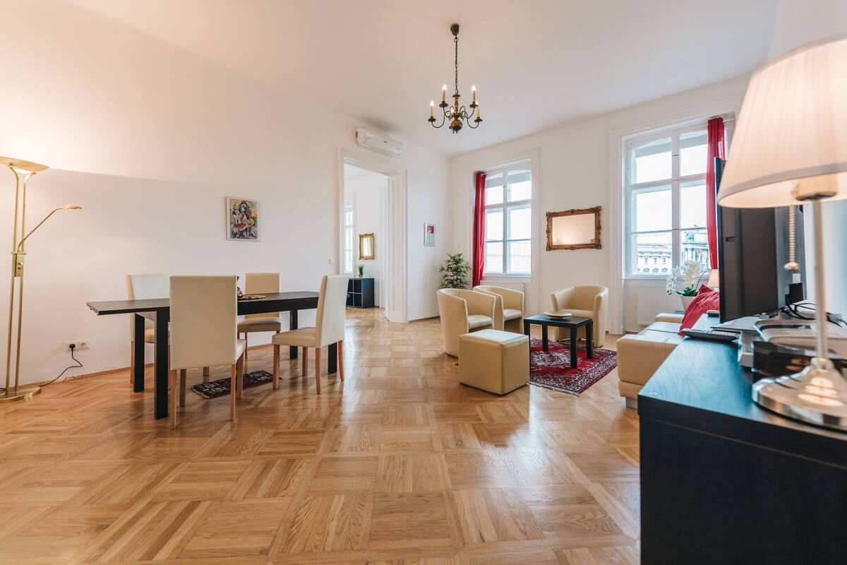 A modern living room with a dining area, wooden flooring, and a chandelier.