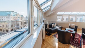Een moderne woonkamer met een groot dakvenster, een zwarte leren bank, een bijzettafeltje en uitzicht op een historisch pand.