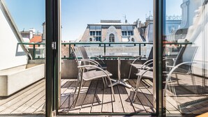 Een dakterras met een tafel en stoelen, een uitzicht op een gebouw met een opvallende architectuur, en een heldere blauwe lucht.